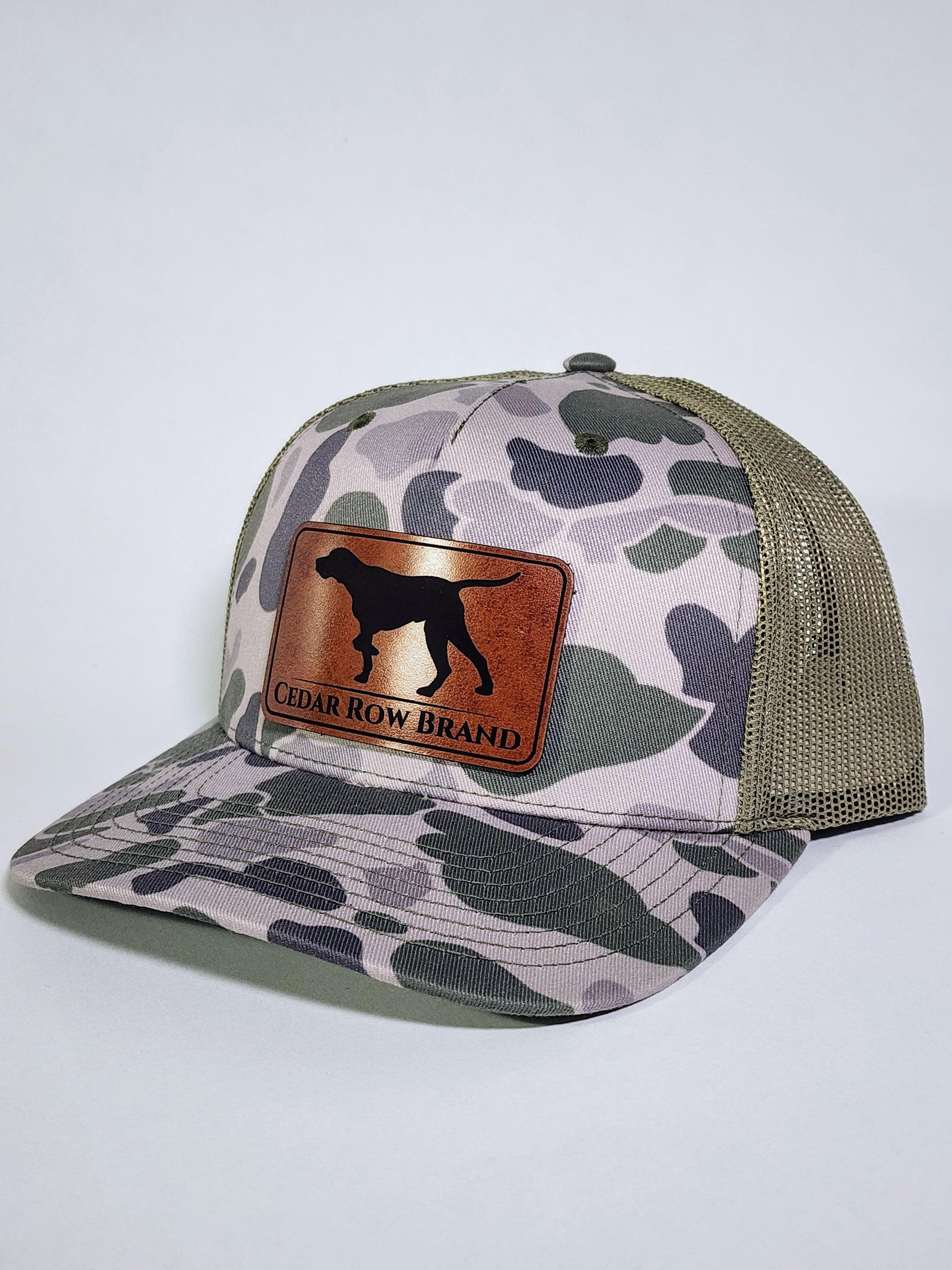 cedar row brand leather patch on a camo trucker hat with a bird dog design